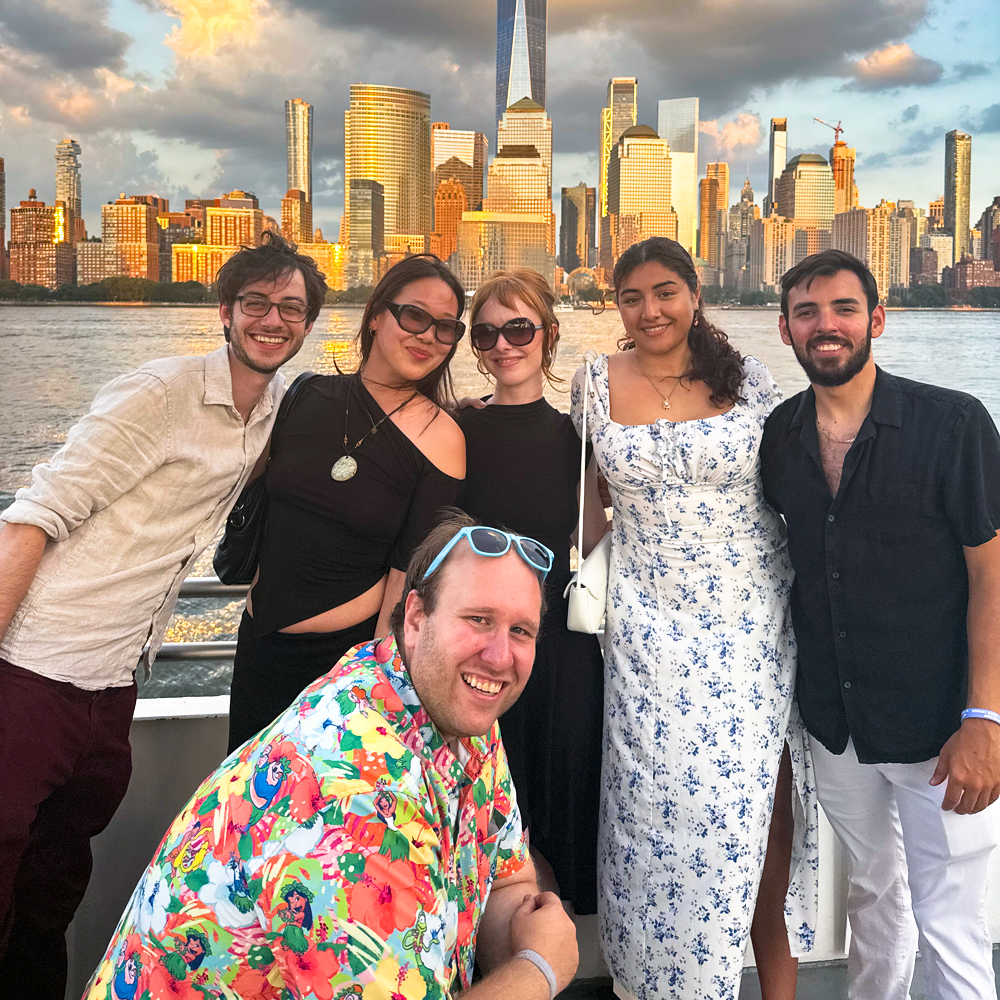 six people standing at the rail of a boat with NYC in the back