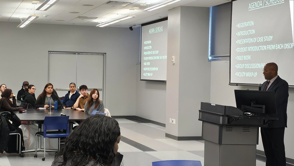 Students, faculty, and staff attend an Interprofessional Education Case Study session as a presenter speaks from a classroom podium.