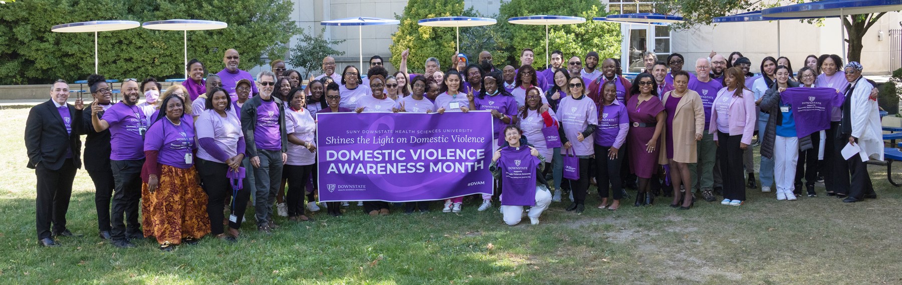 large group photo of people standing outside holding a banner Domestic Violence Awareness Month