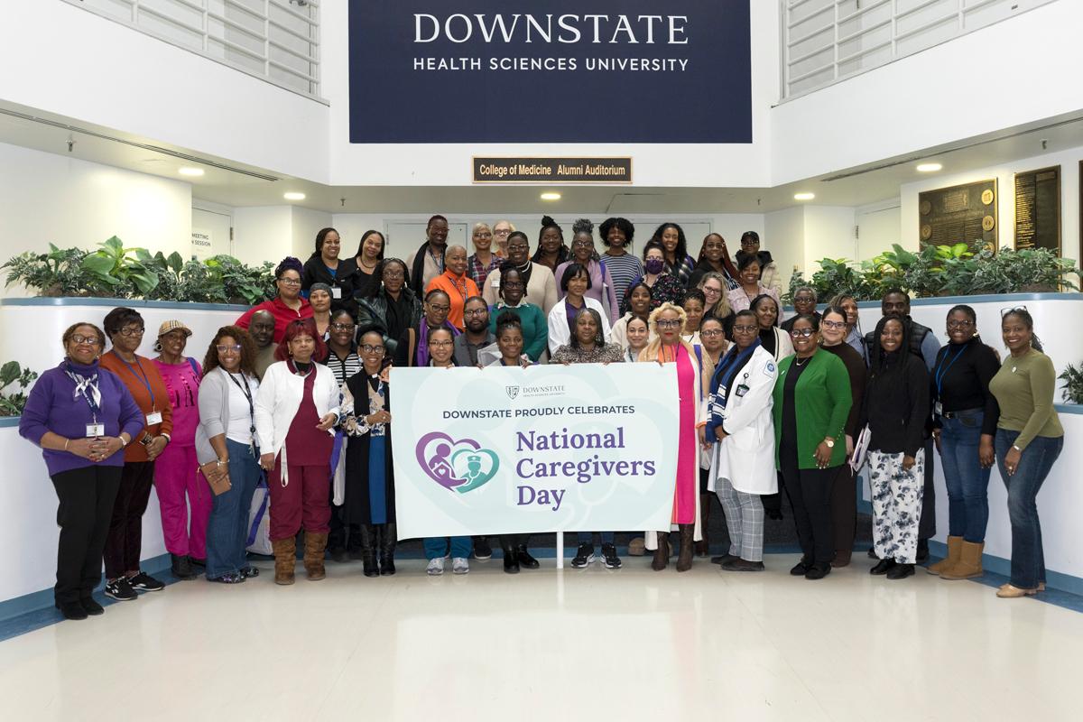 Group photo of people posing on steps holding a banner saying Downstate Proudly Celebrates National Caregivers Day