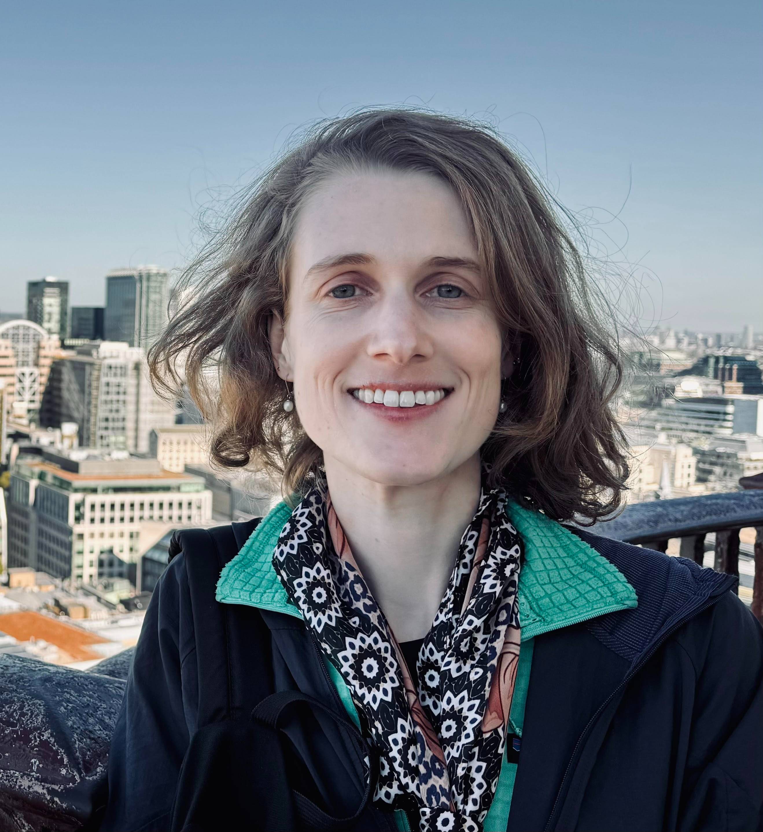 Smiling light skinned young woman with glasses leaning against a concrete wall.