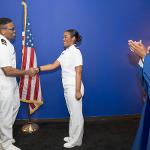 President Riley in Commencement robe applauding Sierrah Grigsby in dress whites along with another naval officer in dress whites.